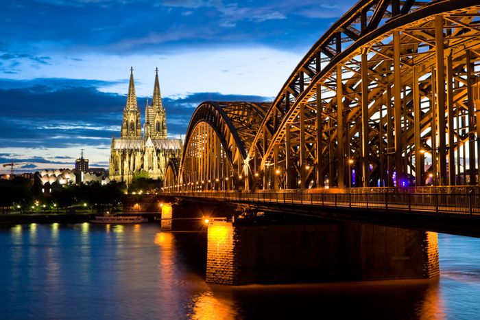 Der Kölner Dom und die beleuchtete Hohenzollernbrücke am Abend über dem Rhein
